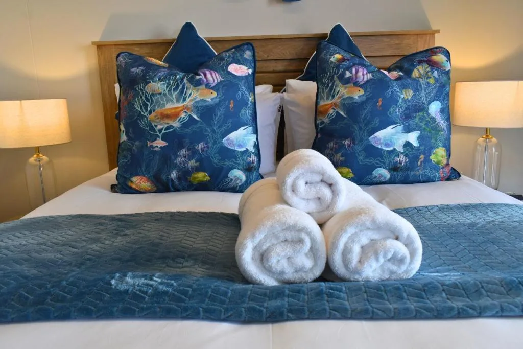 Neatly made bed with ocean-themed pillows and rolled white towels