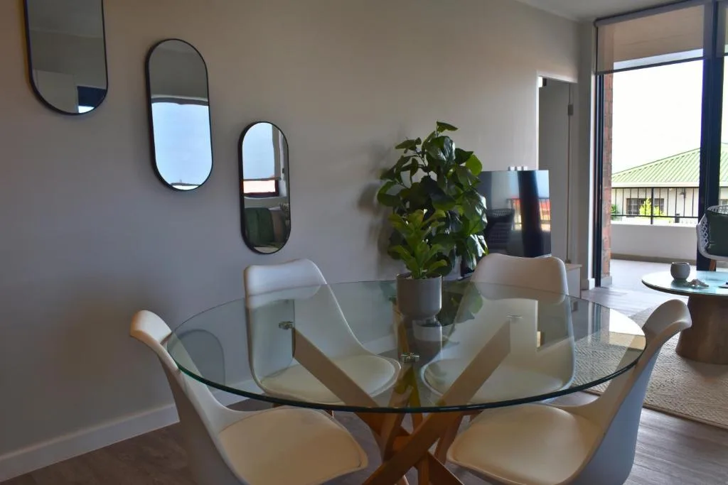 Modern dining area with glass table, cream chairs, and contemporary wall mirrors