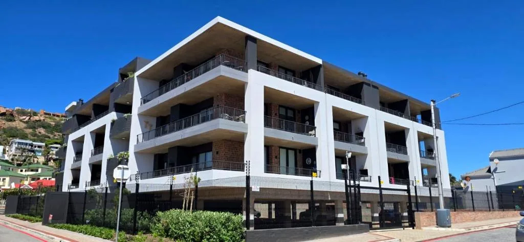 Modern white apartment building with multiple balconies and ground-level parking