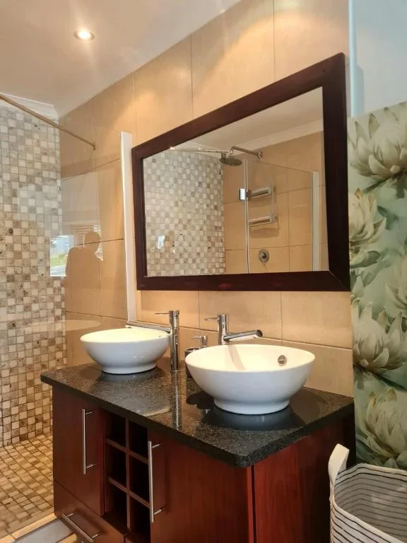 Modern bathroom with dual vessel sinks, large framed mirror, and tiled shower area