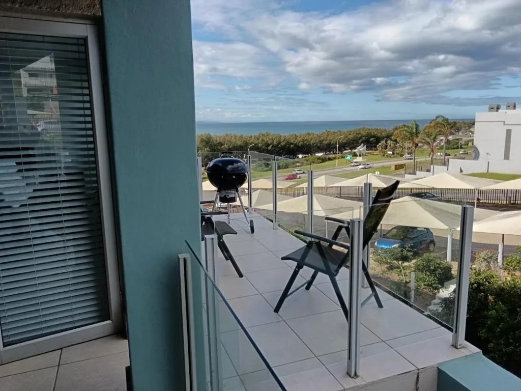 Modern balcony with ocean view, lounge chairs, and braai grill