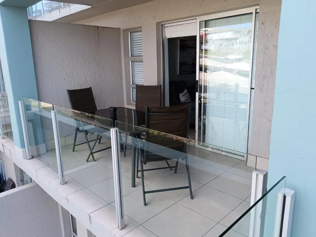 Balcony with glass railing, seating chairs, and sliding glass doors