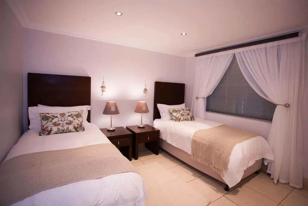 Twin bedroom with dark headboards, white linens, and warm lighting