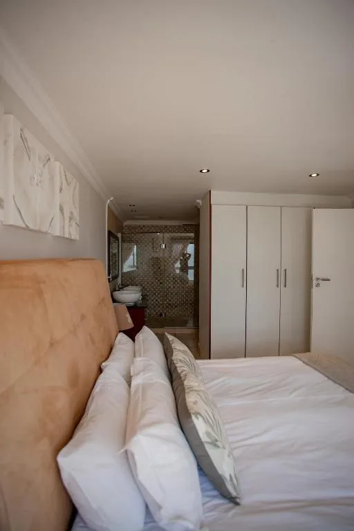 Modern bedroom with white pillows, wooden headboard, and en-suite bathroom visible