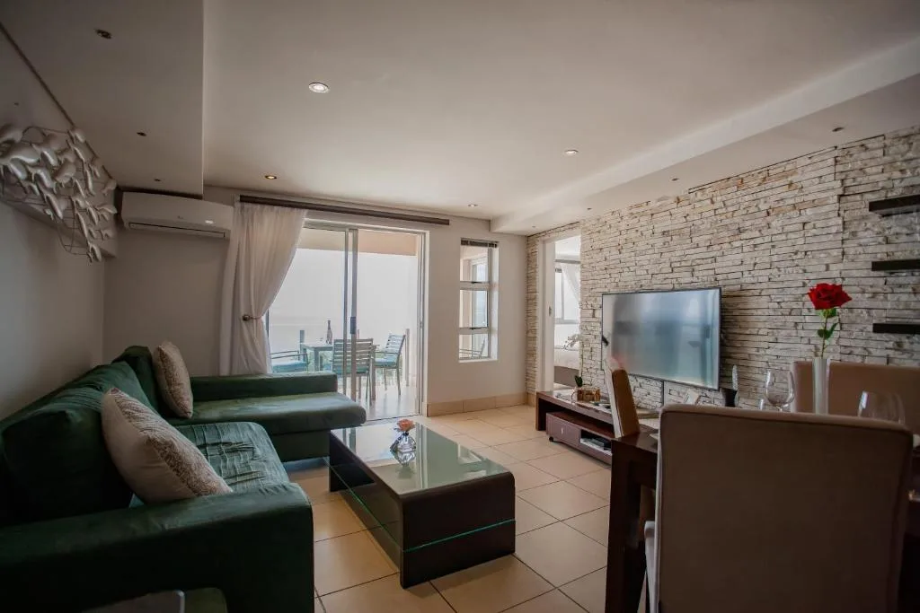 Modern lounge with green sofa, TV, ocean view through glass doors