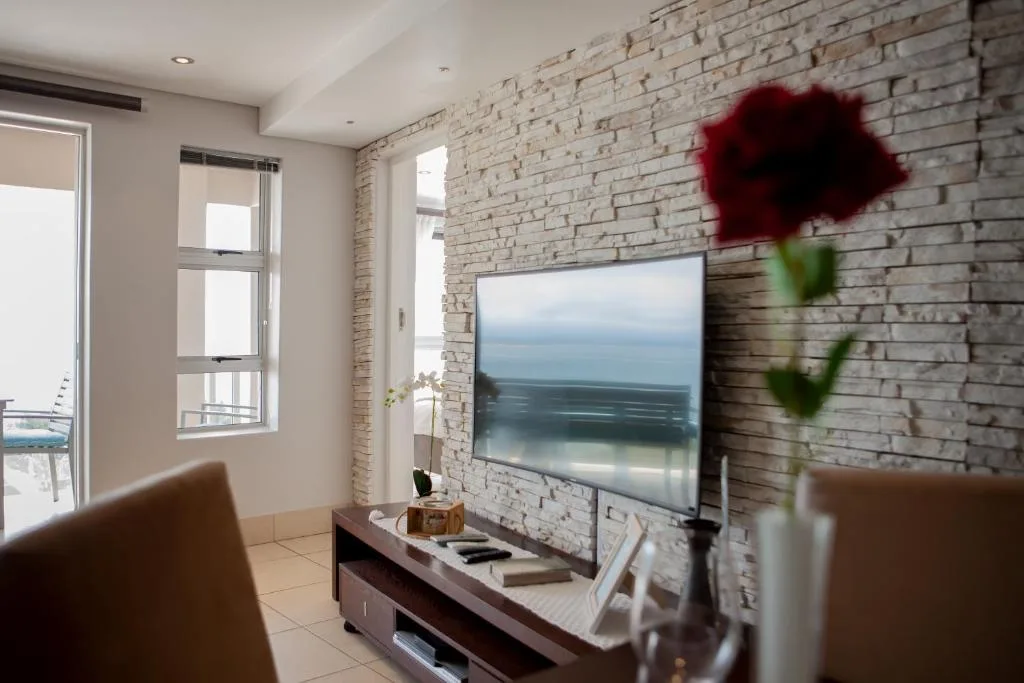 Modern lounge with TV on brick wall, ocean view displayed on screen