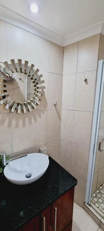 Modern bathroom with circular mirror, white sink, and tiled shower enclosure