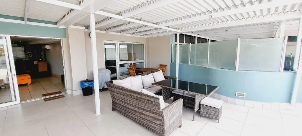 Covered patio area with wicker furniture and ocean views through glass doors