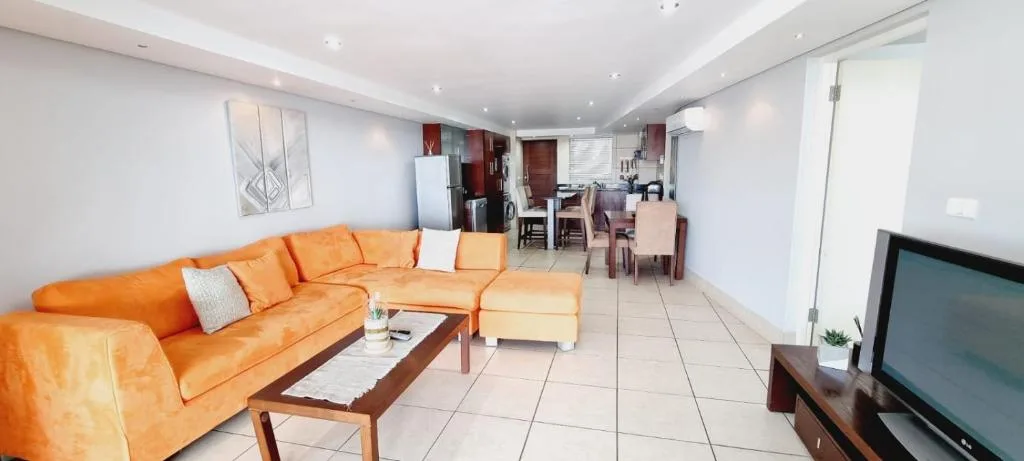 Open-plan lounge with orange leather sofa and dining area beyond