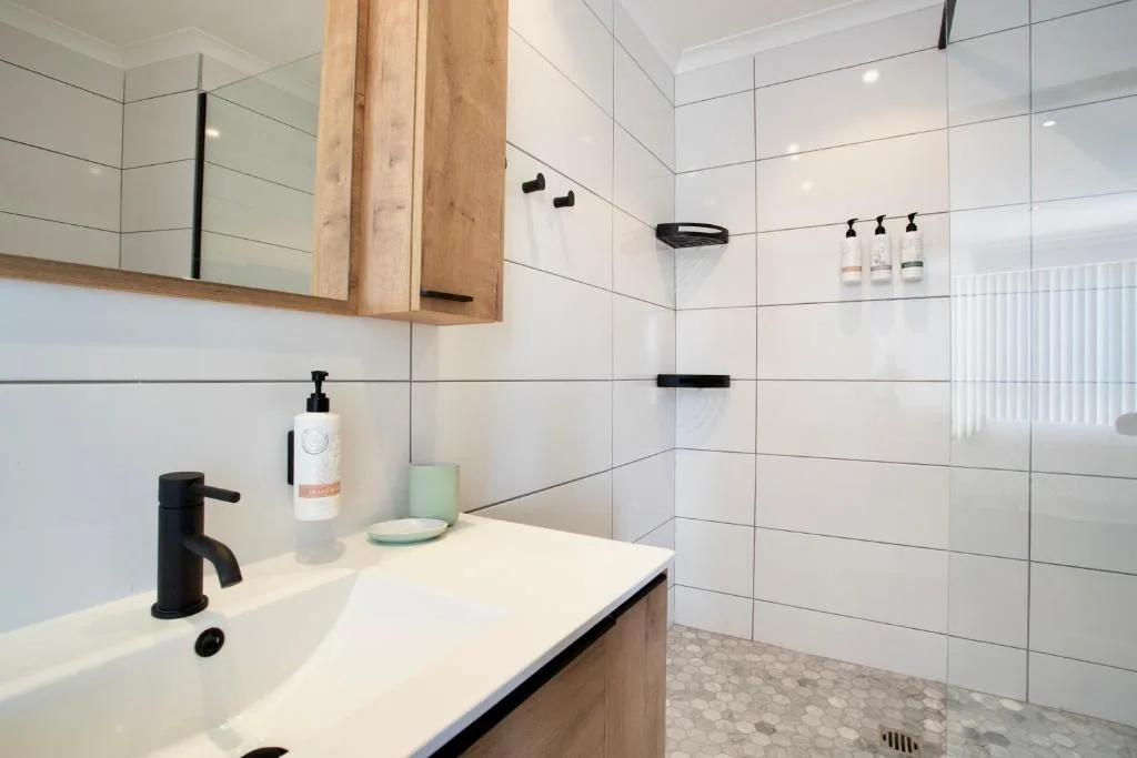 Modern bathroom with white tile walls, black fixtures, and wooden vanity cabinet