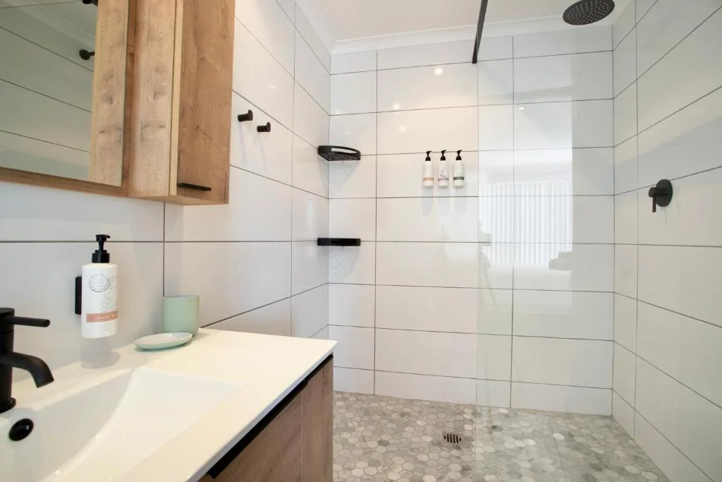 Modern bathroom with white tile walls, walk-in shower, wooden vanity cabinet