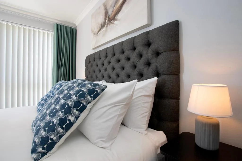 Bedroom with dark tufted headboard, white pillows, blue patterned cushion