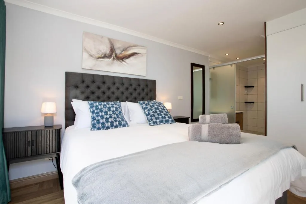 Modern bedroom with queen bed, dark headboard, and ensuite bathroom visible