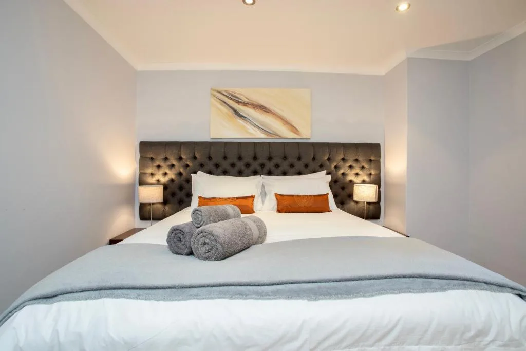 Modern bedroom with tufted headboard, white bedding, and rolled towels