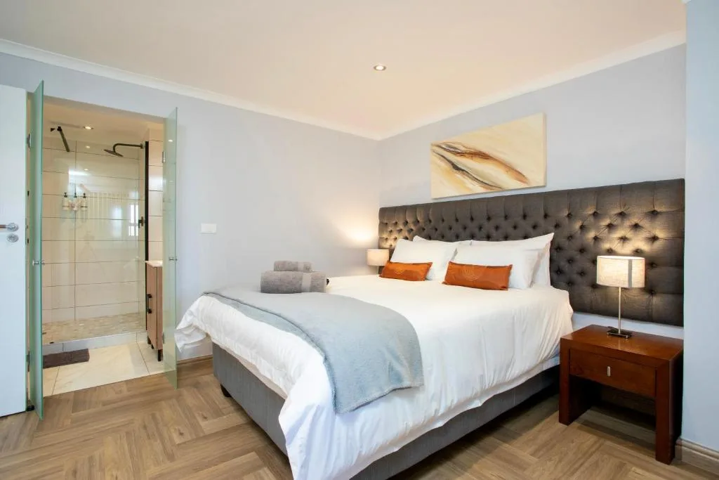 Modern bedroom with king bed, dark upholstered headboard, and ensuite bathroom