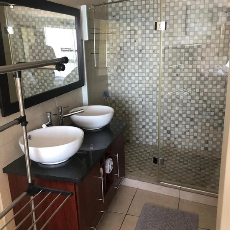 Modern bathroom with dual vessel sinks, dark vanity, and glass shower enclosure