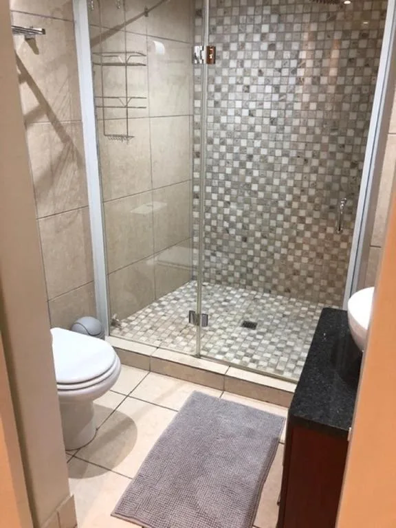 Modern bathroom with walk-in shower, mosaic tiles, and white toilet fixture
