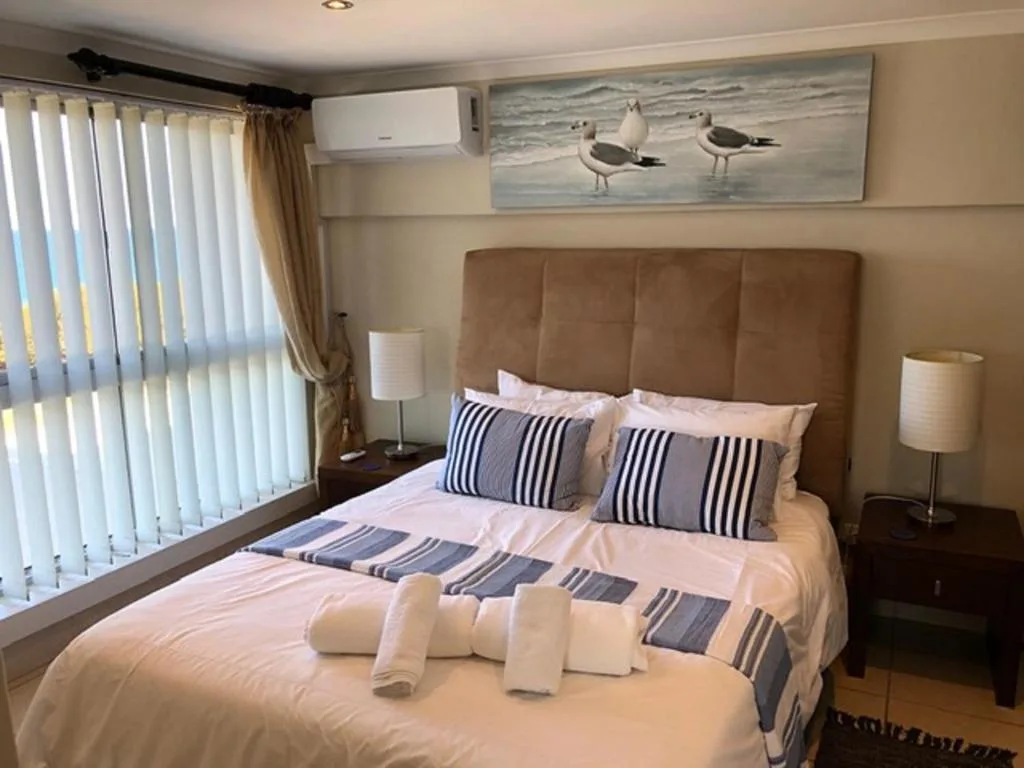 Modern bedroom with queen bed, brown headboard, striped pillows, ocean view artwork