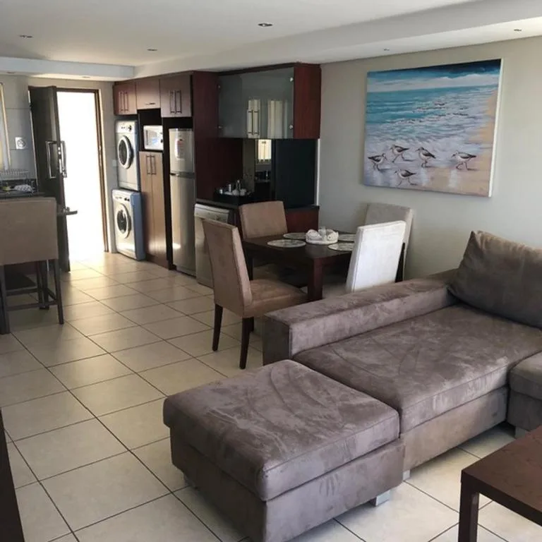 Open-plan lounge with gray sofa, dining area, and integrated kitchen appliances