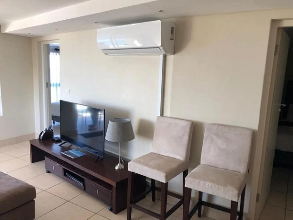 Modern living room with flat-screen TV, dining chairs, and air conditioning unit