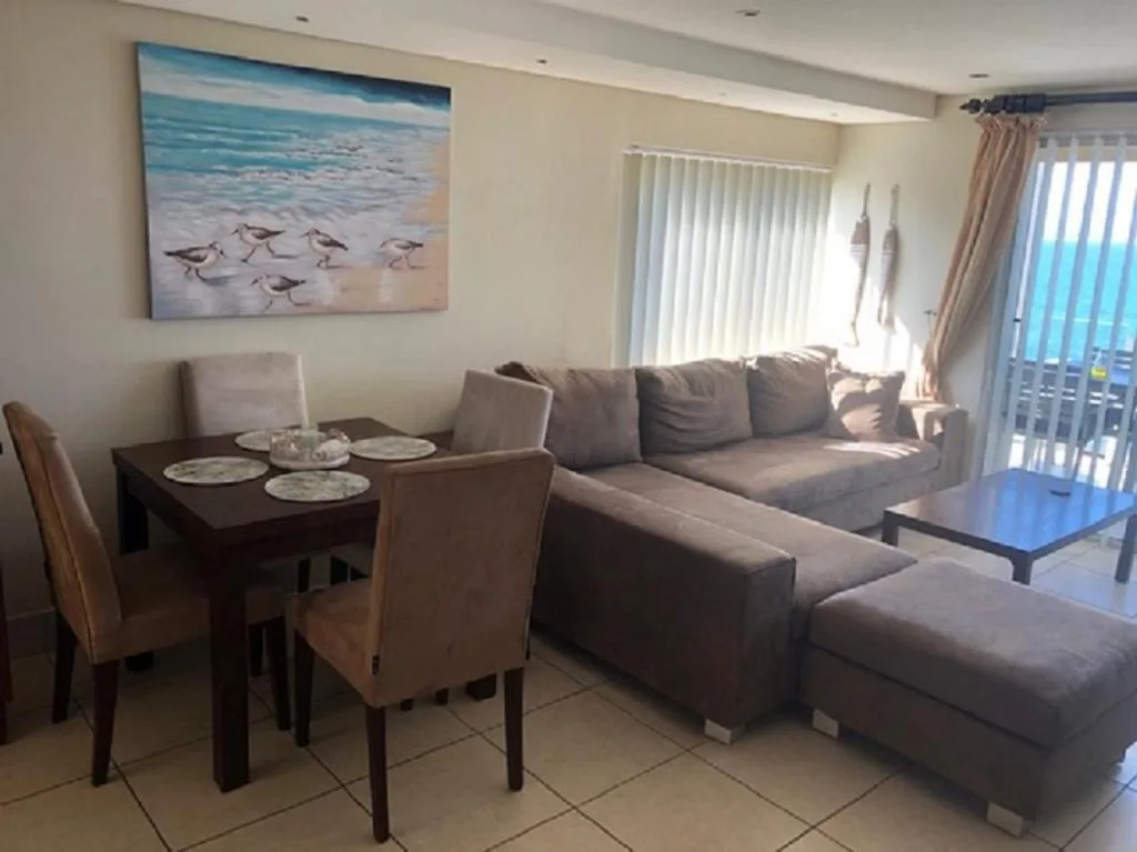 Open-plan lounge and dining area with gray sofa, dining table, and ocean artwork