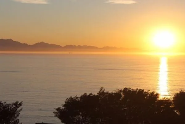 Golden sunrise over calm ocean with distant mountains silhouetted