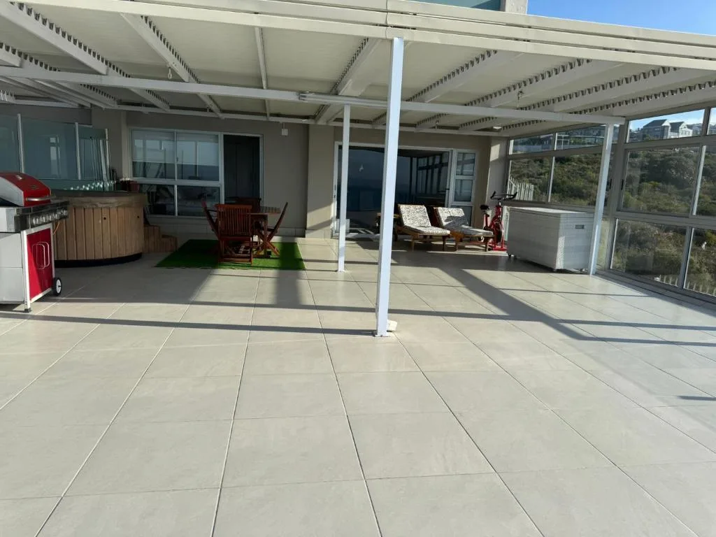 Spacious covered patio with braai area, seating, and panoramic windows overlooking garden
