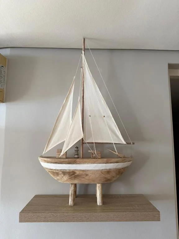 Wooden sailboat model with white canvas sails on shelf