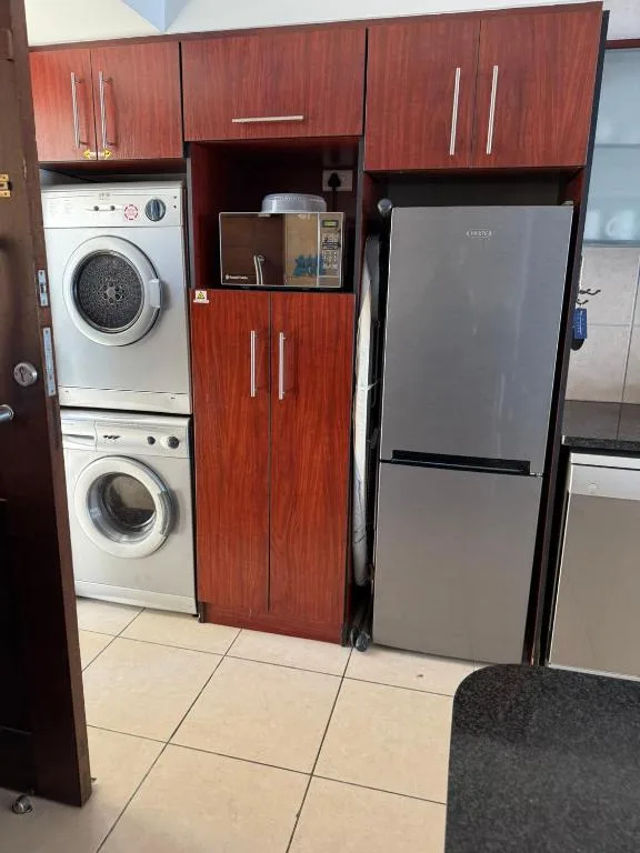Modern kitchen with red cabinetry, stacked washing machines, and stainless steel refrigerator