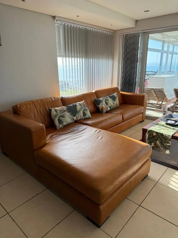 Spacious lounge with tan leather sectional sofa and ocean views through large windows