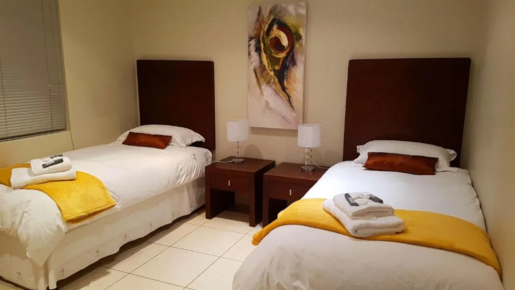 Twin bedroom with white linens, yellow accents, dark headboards, and artwork