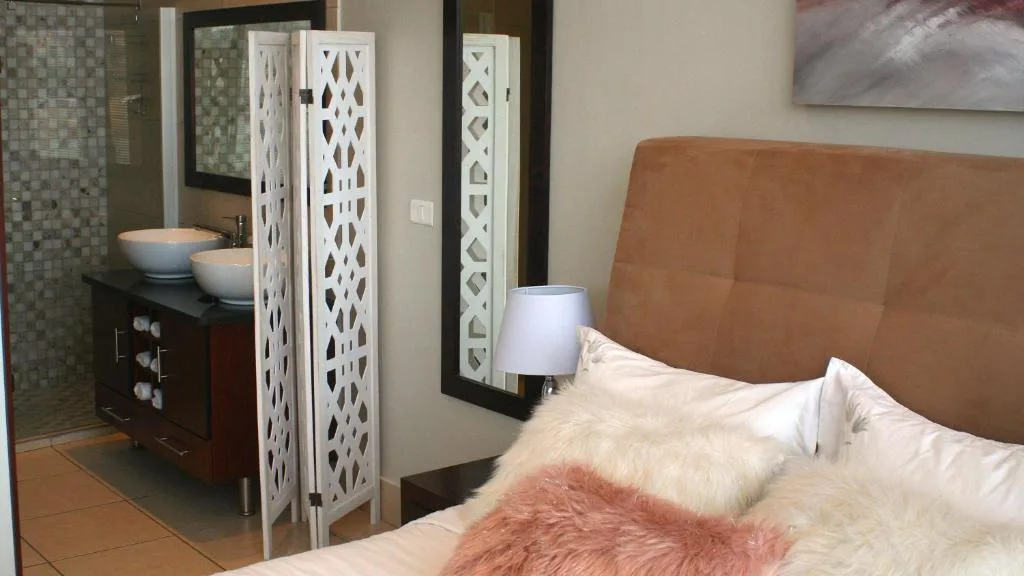 Bedroom with tan leather headboard, white pillows, and ensuite bathroom visible