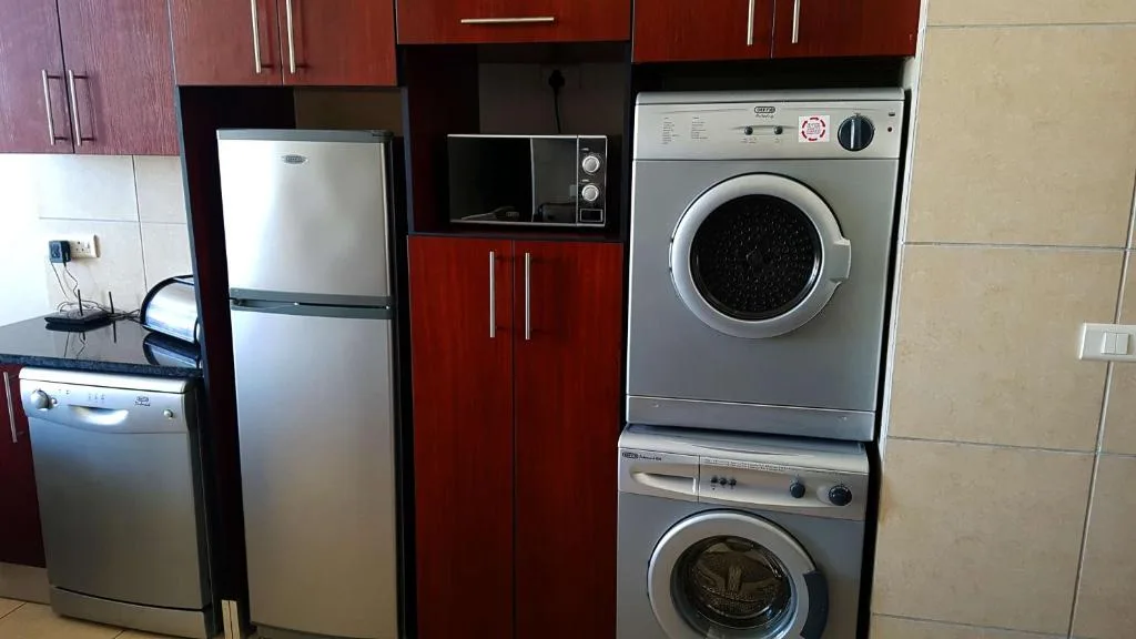 Modern kitchen with stacked washing machines, refrigerator, and red cabinetry