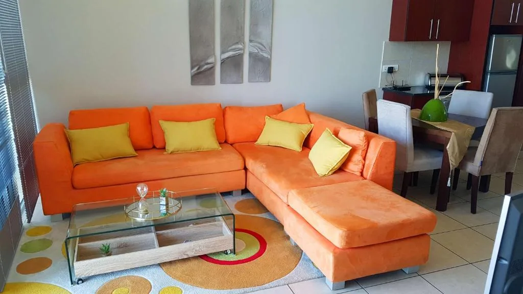 Bright orange sectional sofa with yellow pillows and glass coffee table