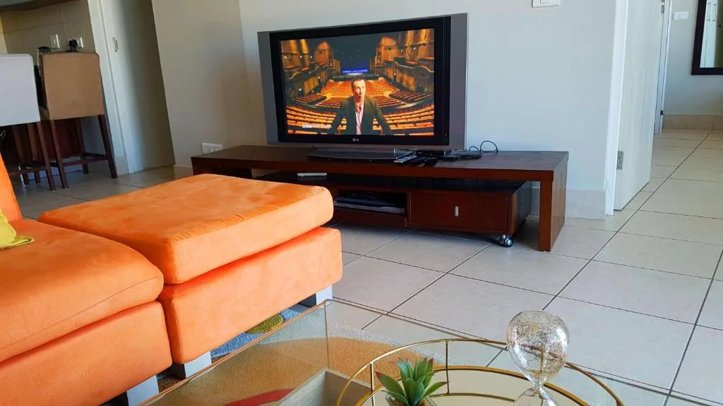 Spacious lounge with orange sofa facing wall-mounted television and entertainment unit