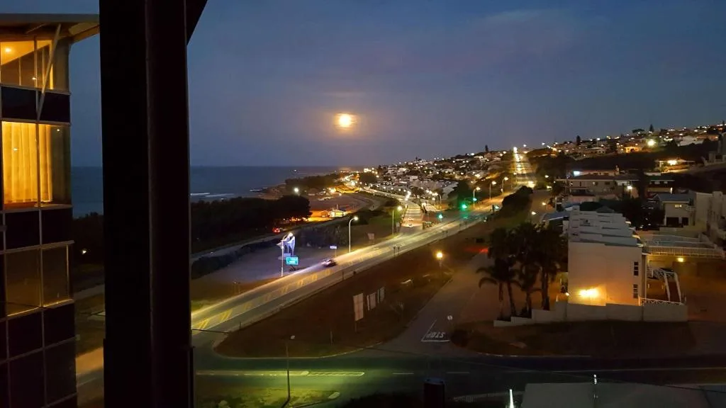 Moonlit coastal town vista with illuminated hillside homes and ocean horizon
