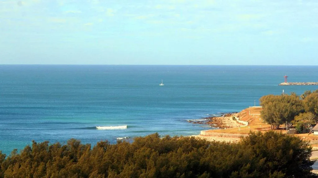 Panoramic ocean view with beach, sailboat, and coastal cliffs