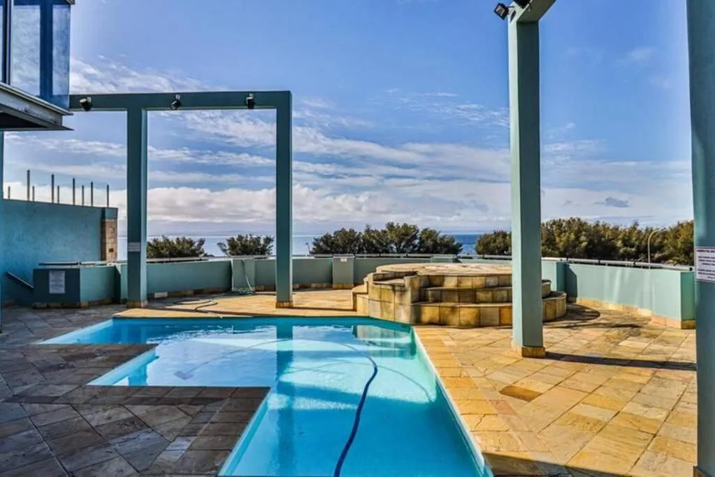 Rectangular swimming pool on sunny deck with ocean view beyond