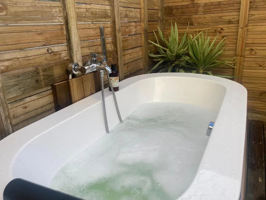 Luxurious outdoor bathtub with hand shower and wooden privacy screens