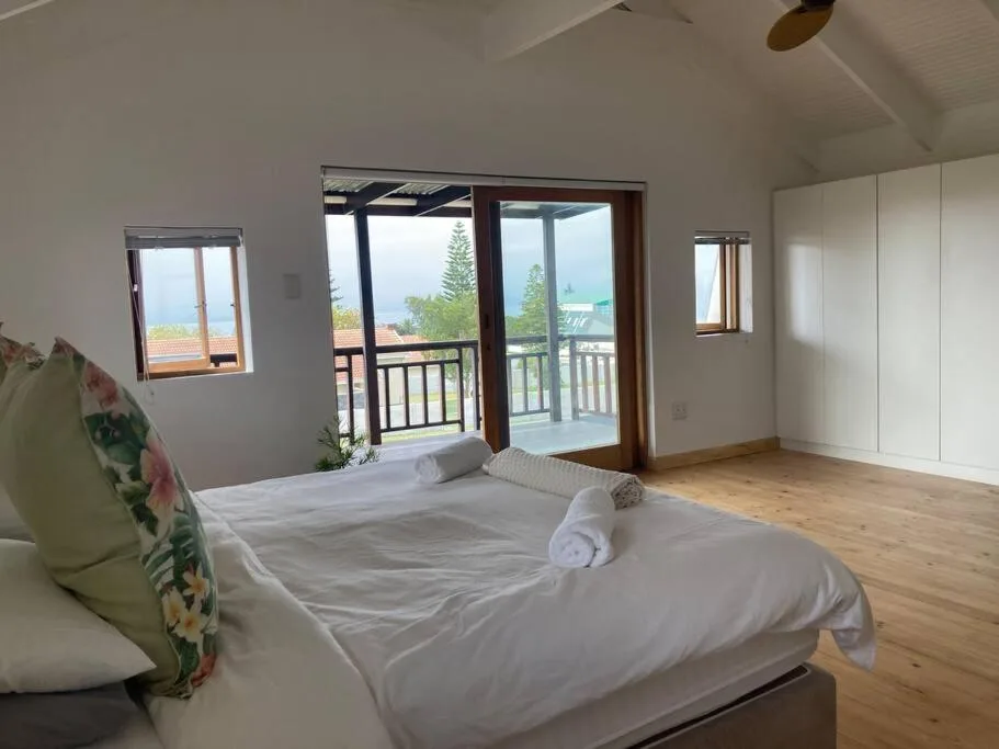Bright bedroom with double bed and panoramic bay views through glass doors