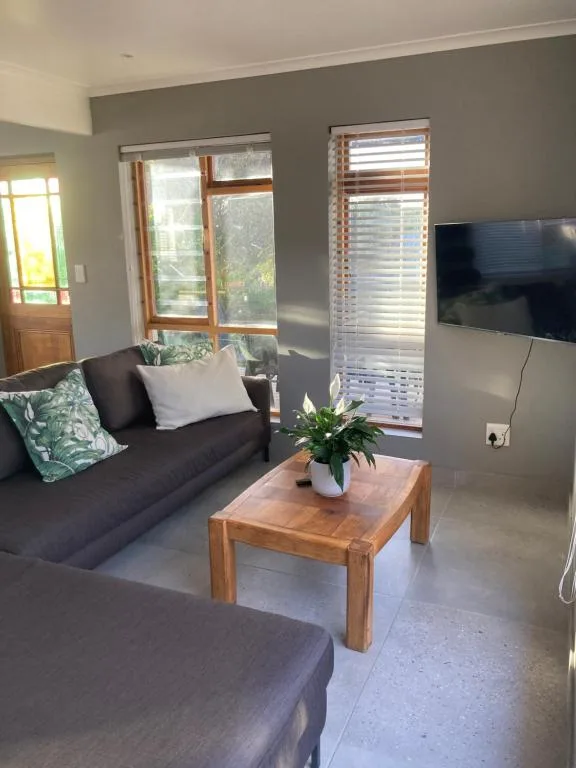 Modern lounge with dark sofa, wooden table, wall-mounted TV, and garden views