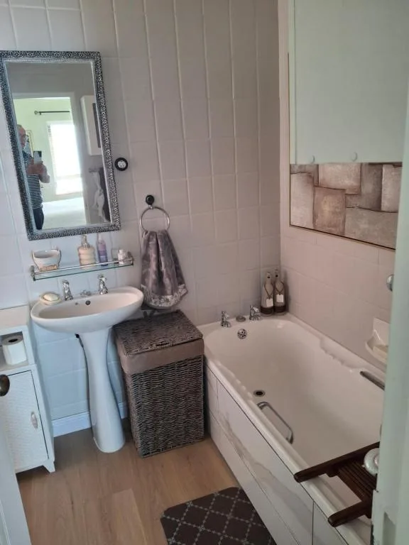 Bathroom with pedestal sink, mirror, and bathtub with toiletries