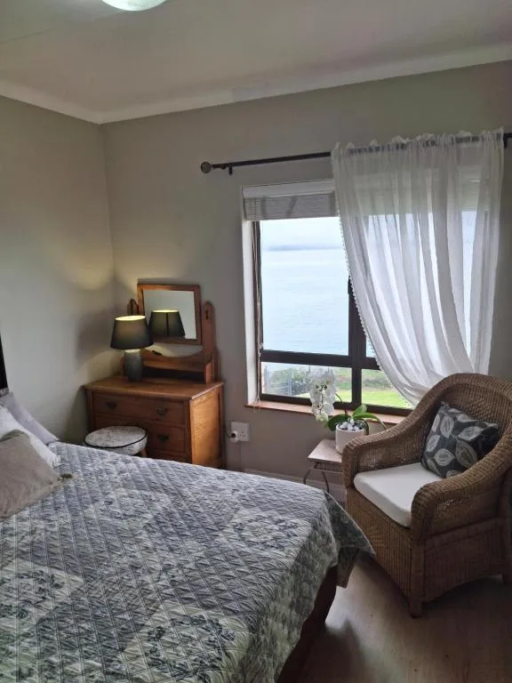 Bright bedroom with bed, wooden dresser, and lagoon views through glass doors
