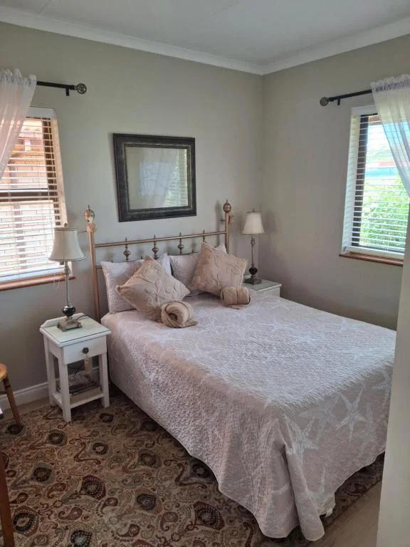 Bright bedroom with queen bed, white nightstands, and windows
