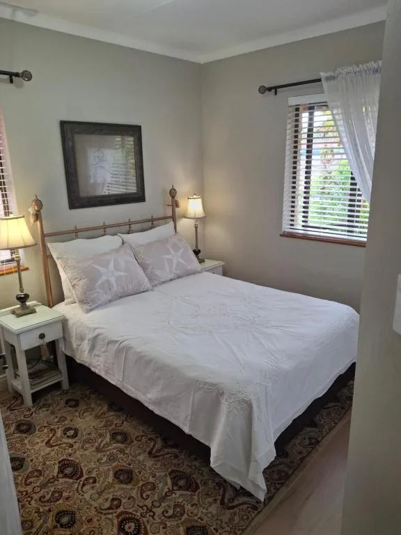 Bright bedroom with queen bed, white bedding, and natural light from window