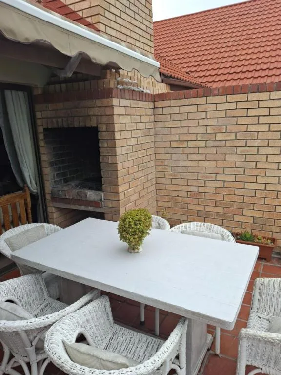 Outdoor patio with white dining table, wicker chairs, and brick fireplace