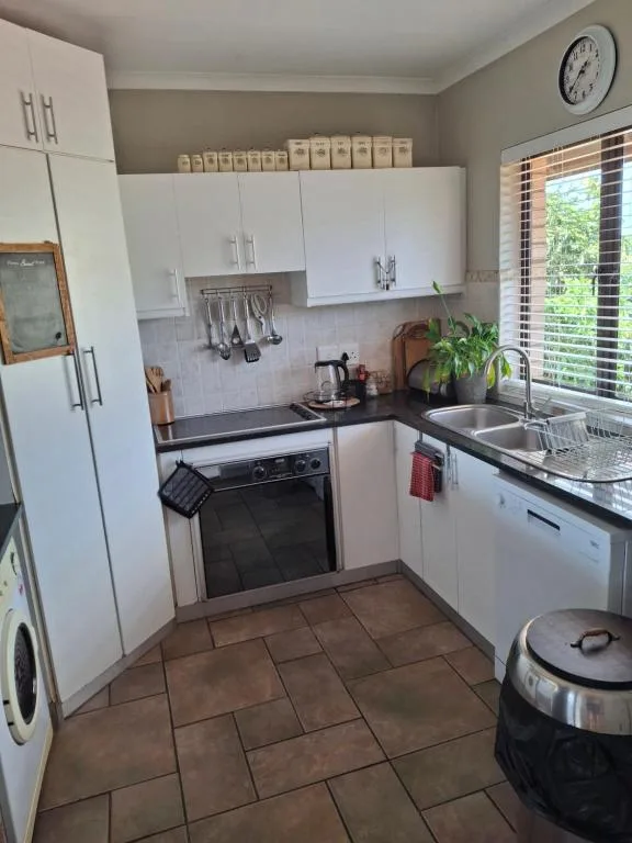 Compact white kitchen with black countertops, stove, sink, and storage cabinets