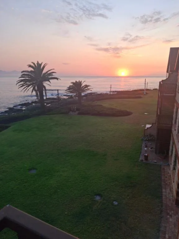 Sunset over ocean with palm trees and manicured lawn below
