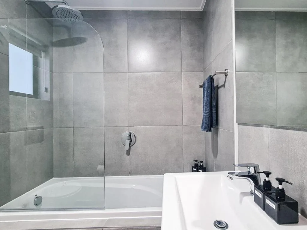Modern bathroom with rainfall showerhead, glass partition, and vanity sink