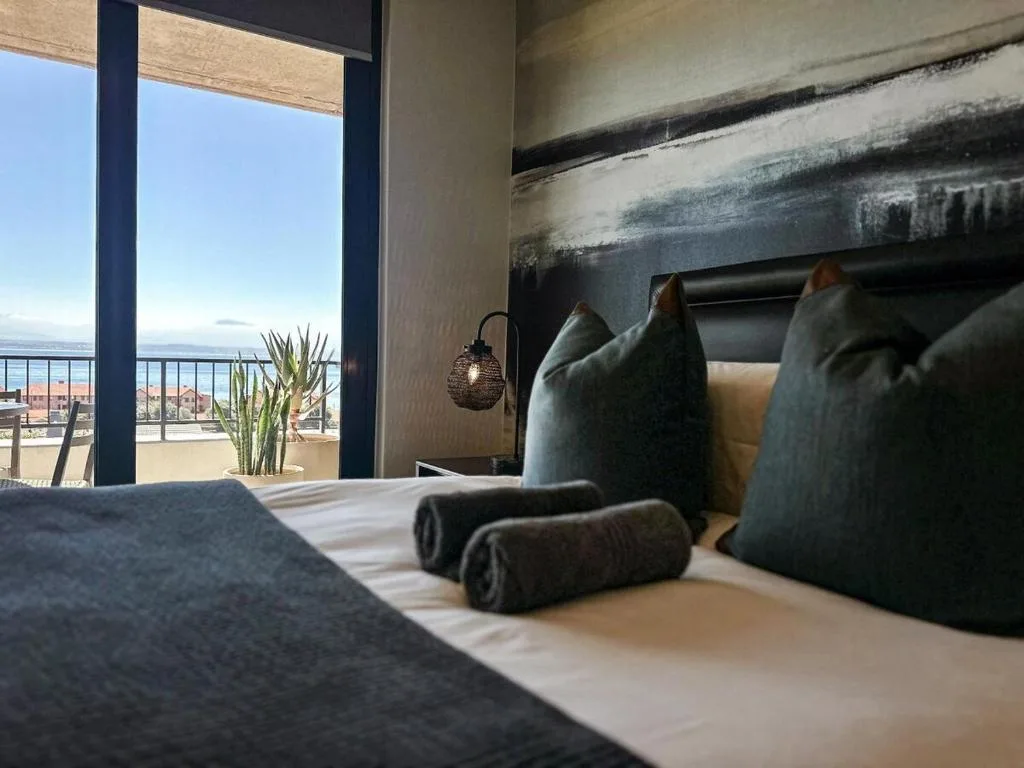 Modern bedroom with coastal view through floor-to-ceiling windows overlooking bay